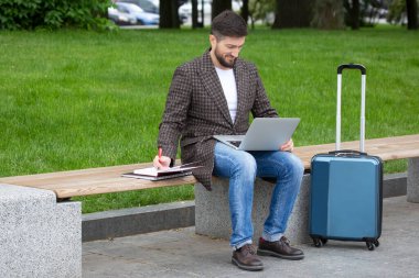 Başarılı bir işadamı, şehir bankında oturuyor ve belgeler ve dizüstü bilgisayarla iş yapıyor.