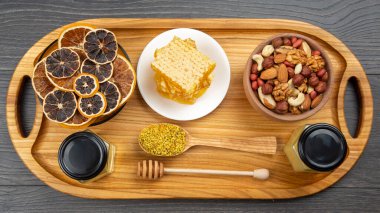 Çeşit çeşit fındık ve çeşitli kurutulmuş narenciye meyveleri ve mutfak tahtasının üzerinde taze bal peteği ve polen. İnsan vücudu için yararlı vitamin yiyeceği