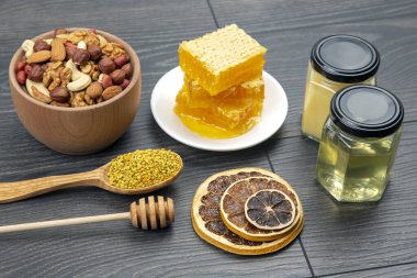Çeşit çeşit fındık ve çeşitli kurutulmuş narenciye meyveleri ve mutfak tahtasının üzerinde taze bal peteği ve polen. İnsan vücudu için yararlı vitamin yiyeceği