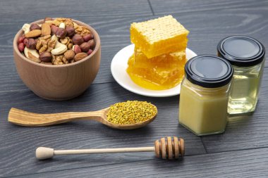 Çeşit çeşit fındık ve çeşitli kurutulmuş narenciye meyveleri ve mutfak tahtasının üzerinde taze bal peteği ve polen. İnsan vücudu için yararlı vitamin yiyeceği