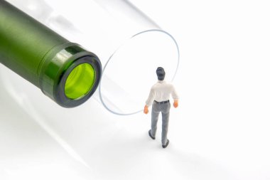 Minyatür insanlar. Alkol bağımlılığı sorunu kavramı. Bir alkolik, şarap şişesinin yanındaki bardağın kenarında durur.