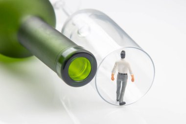 Minyatür insanlar. Alkol bağımlılığı sorunu kavramı. Bir alkolik, şarap şişesinin yanındaki bardağın kenarında durur.