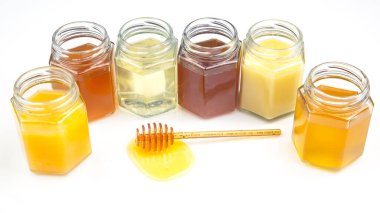 Taze ballı kaşık ve beyaz arka planda farklı bal türleri olan kavanozlar. organik vitamin yiyeceği
