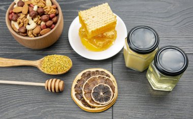 Çeşit çeşit fındık ve çeşitli kurutulmuş narenciye meyveleri ve mutfak tahtasının üzerinde taze bal peteği ve polen. İnsan vücudu için yararlı vitamin yiyeceği