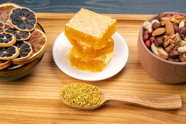 Çeşit çeşit fındık ve çeşitli kurutulmuş narenciye meyveleri ve mutfak tahtasının üzerinde taze bal peteği ve polen. İnsan vücudu için yararlı vitamin yiyeceği