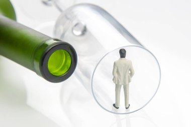 Minyatür insanlar. Alkol bağımlılığı sorunu kavramı. Bir alkolik, şarap şişesinin yanındaki bardağın kenarında durur.