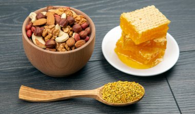 Çeşit çeşit fındık ve çeşitli kurutulmuş narenciye meyveleri ve mutfak tahtasının üzerinde taze bal peteği ve polen. İnsan vücudu için yararlı vitamin yiyeceği