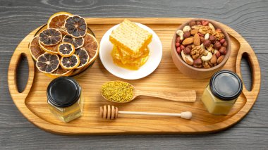 Çeşit çeşit fındık ve çeşitli kurutulmuş narenciye meyveleri ve mutfak tahtasının üzerinde taze bal peteği ve polen. İnsan vücudu için yararlı vitamin yiyeceği
