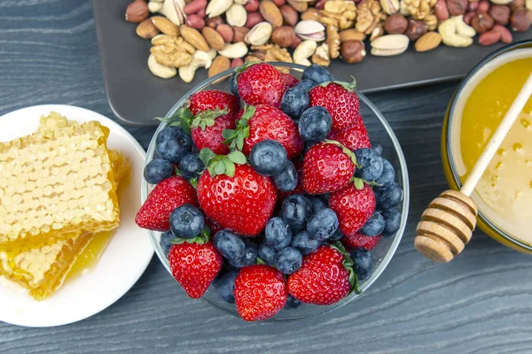 Tahta arka planda taze bal, fındık, çilek ve yaban mersini. sağlıklı organik vitamin yiyeceği.