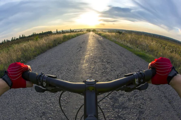 Eller direksiyonda, gün batımına doğru bisiklet sürüyor.