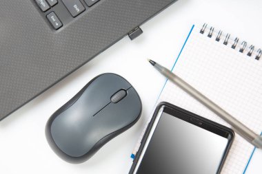 Bilgisayar kablosuz fare, kalem ve not defteri beyaz bir masada yakın plan dizüstü bilgisayarın yanında. Ofis işleri için eşyalar