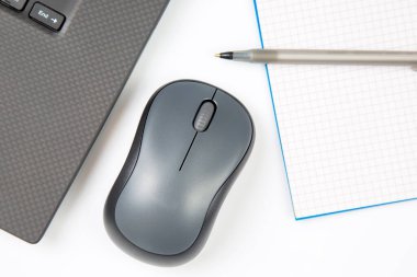 Bilgisayar kablosuz fare, kalem ve not defteri beyaz bir masada yakın plan dizüstü bilgisayarın yanında. Ofis işleri için eşyalar