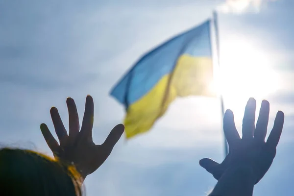 Raised hands to the sky against the background of the flag of Ukraine. Prayer for help and