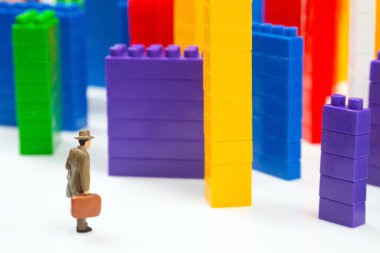 Minyatür insanlar. Plastik bir inşaatçının renkli bloklarının yanında beyaz arka planda, çok katlı binalar şeklinde duran insan figürleri. Modern binalar ve evler kavramı