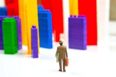 Minyatür insanlar. Plastik bir inşaatçının renkli bloklarının yanında beyaz arka planda, çok katlı binalar şeklinde duran insan figürleri. Modern binalar ve evler kavramı