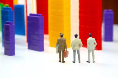 Minyatür insanlar. Plastik bir inşaatçının renkli bloklarının yanında beyaz arka planda, çok katlı binalar şeklinde duran insan figürleri. Modern binalar ve evler kavramı