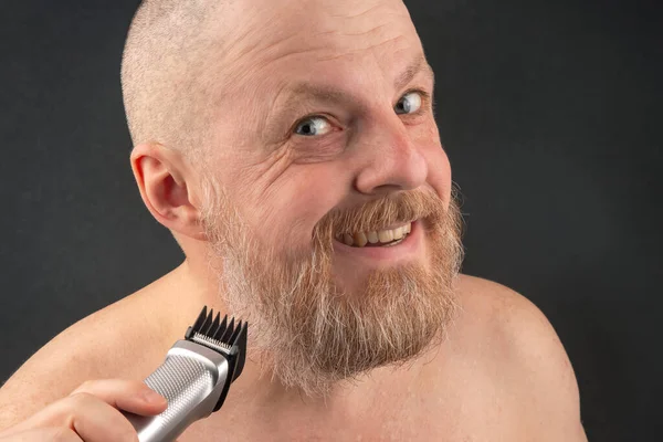 Bearded man with trimmer to adjust beard in hand. grooming and fashionable style barbershop. Beard length correction