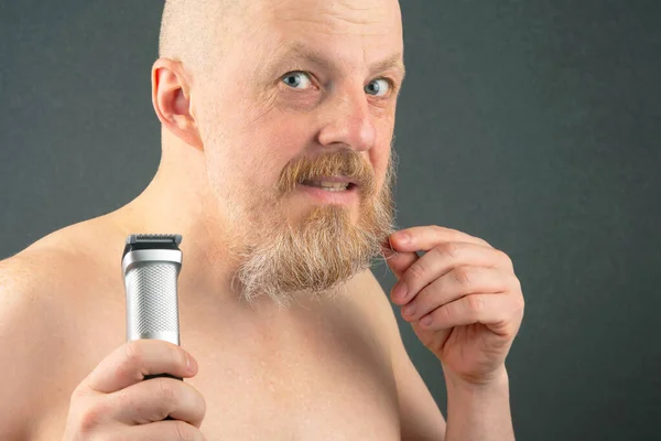 Bearded man with trimmer to adjust beard in hand. grooming and fashionable style barbershop. Beard length correction