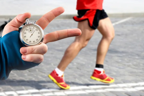 Measuring The Running Speed Of An Athlete Using A Mechanical Stopwatch.  Hand With A Stopwatch On The Background Of The Legs Of A Runner. Stock  Photo, Picture and Royalty Free Image. Image