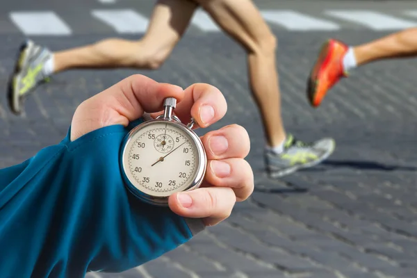 measuring the running speed of an athlete using a mechanical stopwatch. hand with a stopwatch on the background of the legs of a runner.