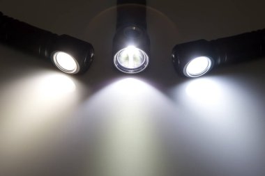 Karanlık bir arkaplanda farklı fenerlerin ışık demetleri vardı. Işık sıcaklığının karşılaştırılması. kamp ve ev eşyası.