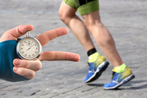 Measuring The Running Speed Of An Athlete Using A Mechanical Stopwatch.  Hand With A Stopwatch On The Background Of The Legs Of A Runner. Stock  Photo, Picture and Royalty Free Image. Image