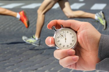 Mekanik kronometre kullanan bir sporcunun hızını ölçmek. Bir koşucunun arka planında kronometre olan bir el. ayaklar çalışıyor