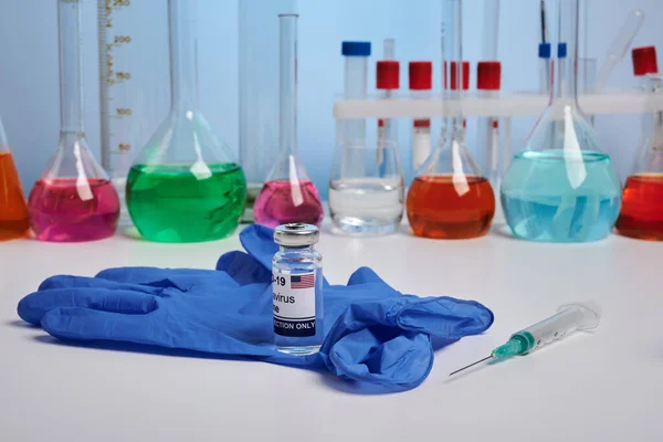 Американская ковидная вакцина и перчатка на химическом столе — стоковое фото