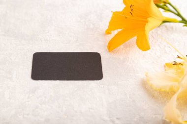 Gri çimento arka planda turuncu zambak çiçekli siyah kağıt kartvizit modeli. Boş, yan görüş, kopyalama alanı, natürmort hayat. bahar konsepti.