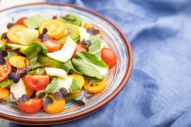 Pac choi lahana, kivi, domates, kumkatlı vejetaryen salatası, beyaz beton arka planda mikroyeşil lahanalar ve mavi keten tekstil. Yan görünüm, yakın görünüm, seçici odak.
