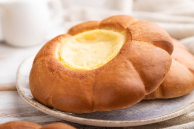 Beyaz ahşap arka planda bir fincan kahveli ekşi kremalı çörek ve keten tekstil. Yan görünüm, yakın görünüm, seçici odak.