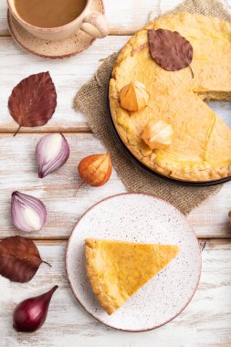 Sonbahar soğanlı turta, yapraklarla süslenmiş ve beyaz ahşap arka planda bir fincan kahve ve keten tekstil. Üst manzara, düz yatak, yakın çekim..