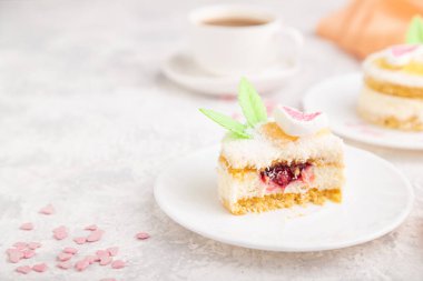 Sütlü, hindistan cevizi kremalı, gri beton arka planda bir fincan kahve ve turuncu tekstil ile süslenmiş kek. Yan görünüm, boşluk kopyala.