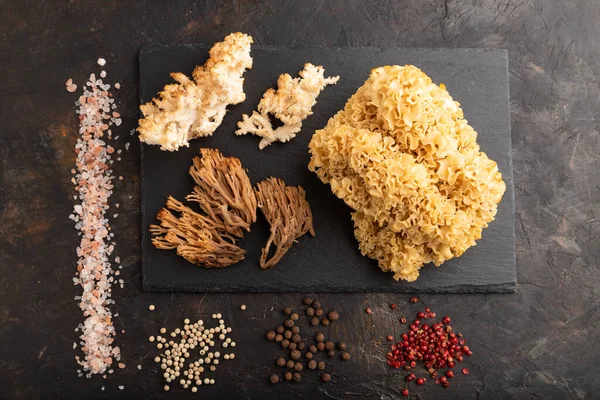 Çiğ Sparassis (Karnabahar Mantarı), Hericium, Clavaria (mercan mantarı) tuz ve baharatlı siyah beton arka planda. Üst manzara, düz uzanma.