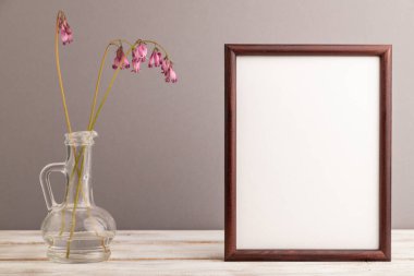 Ahşap çerçeve pembe dicentra, kırık kalp cam içinde gri pastel arka plan. Yan görünüm, kopyalama alanı, modelleme, şablon, bahar, yaz minimalizmi kavramı.