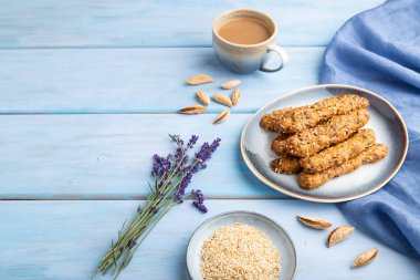 Mevsimlik kurabiyeler ve seramik tabakta badem, bir fincan kahve ve mavi ahşap arka planda mavi keten kumaş. Yan görünüm, boşluk kopyala.