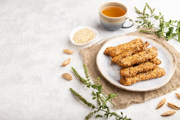 Baharatlı çörekler ve seramik tabakta badem, yeşil çay fincanı ve gri beton arka planda keten tekstil. Yan görünüm, boşluk kopyala.