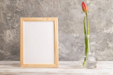 Ahşap çerçeve, gri beton arka planda cam içinde kırmızı lale çiçeği. Yan görünüm, kopyalama alanı, natürmort, model, şablon, bahar, yaz minimalizmi kavramı.