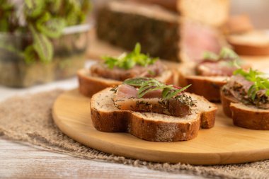 Beyaz ahşap arka plan ve keten tekstil üzerinde kurutulmuş et, kuş ve kişniş mikroyeşil ekmekli sandviç. Yan görünüm, yakın görünüm, seçici odak.