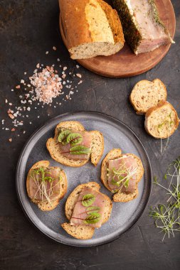Siyah beton arka planda kurutulmuş et, kuş gülü ve kişniş mikroyeşil ekmekli sandviç. Üst görünüm, düz görünüm, yakın çekim.