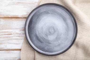 Beyaz ahşap arka planda boş gri seramik tabak ve keten tekstil. Üst manzara, kapat, düz yat..