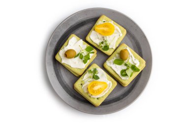 Krem peynirli yeşil krakerli sandviçler ve beyaz arka planda izole edilmiş gri tabakta kiraz domatesleri. Üst görünüm, düz görünüm, yakın çekim.