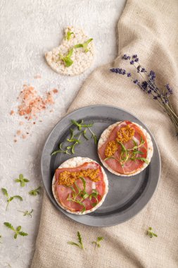 Kurutulmuş et, mikroyeşil ve hardallı pirinç keki sandviçleri gri beton arka plan ve keten tekstil. Üst görünüm, düz görünüm, yakın çekim.