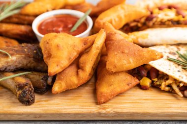 Atıştırmalık şeyler: Nacho, tavuk kanadı, kızarmış kaburga, gri ahşap arka planda kesme tahtasındaki fasulye tortillası. Yan görünüm, yakın görünüm, seçici odak.