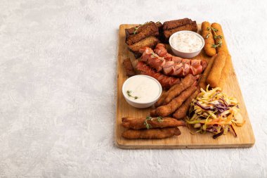 Atıştırmalıklar: sosis, nugget, peynir çubuğu, tost, lahanalı salata gri beton arka planda kesim tahtasında. Yan görünüm, boşluk kopyala.