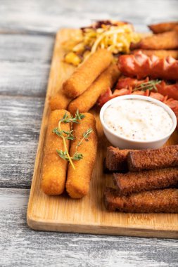 Abur cubur seti: sosis, nugget, peynir çubuğu, tost, lahanalı salata gri ahşap bir arka planda kesim tahtasının üzerinde. Yan görünüm, yakın görünüm, seçici odak.