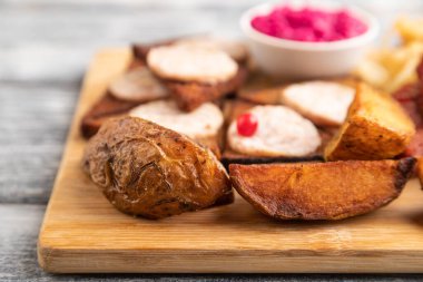 Atıştırmalık şeyler: sosis, tost, lahana turşusu, marine edilmiş soğan ve salatalık, gri ahşap arka planda kesilmiş patates. Yan görünüm, yakın görünüm, seçici odak.