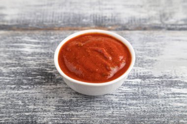 Gri ahşap arka planda domates soslu seramik sos kasesi. Yan görünüm, kapat, boşluğu kopyala.