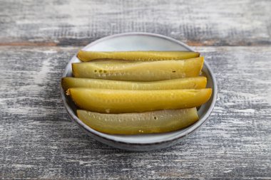 Gri ahşap arka planda mavi seramik tabakta marine edilmiş salatalık. Yan görünüm, kapat.