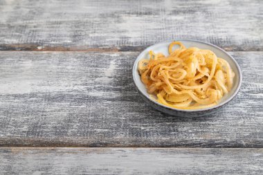 Gri ahşap arka planda mavi seramik tabakta marine edilmiş soğan. Yan görünüm, kapat, boşluğu kopyala.